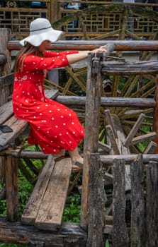 Wullingyuan, China -  August 2019 : Female dressed in a red dress using her legs to pull levers on a wheel of an old Water wheel in Huanglong Yellow Dragon Cave scenic area, Hunan province