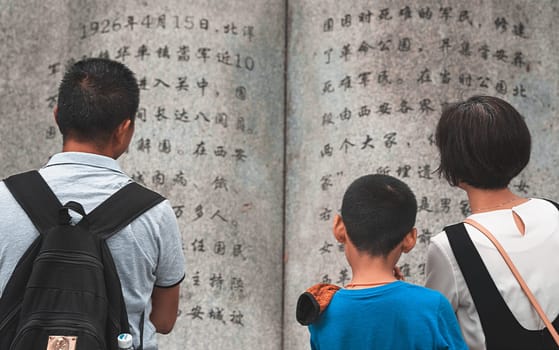 Xian, China -  August 2019 : Family reading text from a page in a large sculpture stone book in Geming Revolution Park, Shaanxi Province