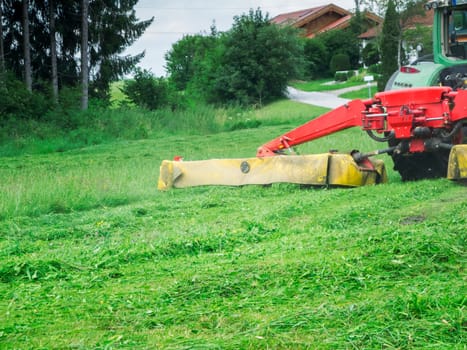 Tractor with grass cutting header at work on a hilly meadow in Bavaria.