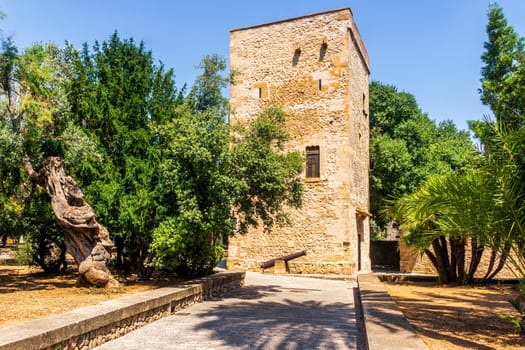 An old square tower in park with cannon, surrounded by palms and trees near main square in Pollenca, Mallorca, Spain