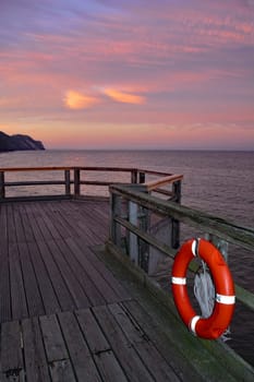 Wooden pier with one  red lifebuoy on the Baltic Sea after sunset, overlooking the sea with copy space