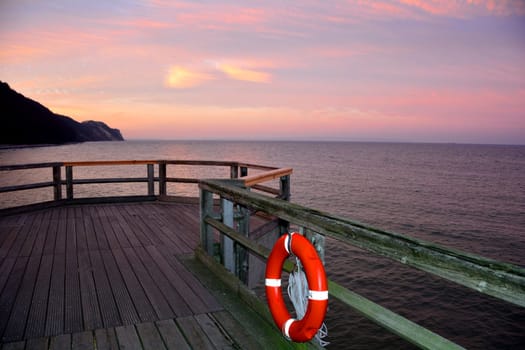 Wooden pier with a red lifebuoy on the Baltic Sea after sunset, overlooking the sea with copy space