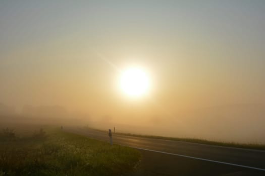 Sunrise with empty asphalt road , in the countryside with copy space, sun and fog