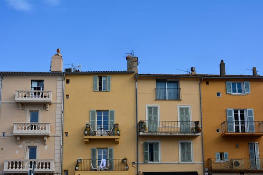 Colored house facade in the historic center of Saint Tropez, France, with balconies and blue sky