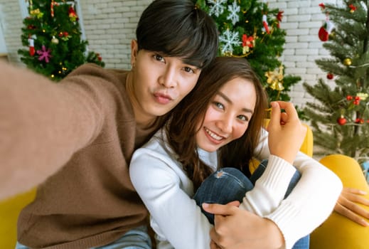 Young asian adult teenager coupletake selfie photographing for celebrateing christmas holiday together in living room with christmas tree decoration.