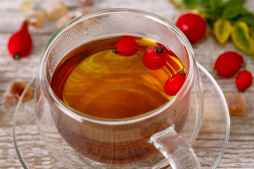 Rosehip tea in a glass cup with rose hips around the cup