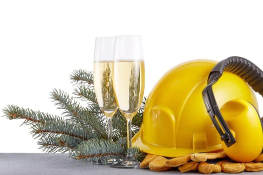 Construction protective clothes (hard hat, gloves and earphones), fir tree branches and two glasses with champagne standing on glittering silver surface. Copy space. New Year and Christmas
