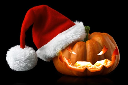 Single orange pumpkin Jack-o-lantern with Christmas Santa hat isolated on black