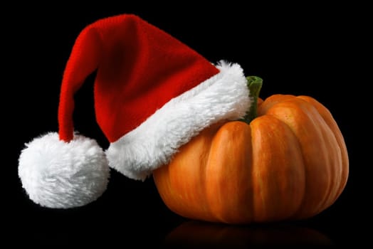 Single orange pumpkin with Christmas Santa hat isolated on black