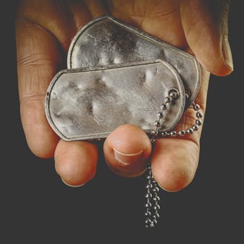 Hand holding blank, old, and worn military dog tags with chain.