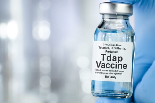 Healthcare concept with a hand in blue medical gloves holding Tap, tetanus, diptheria, and pertussis, vaccine vial