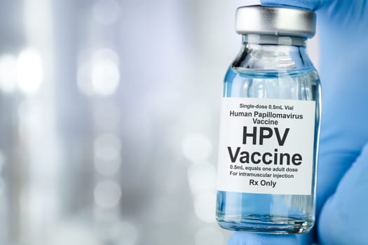 Healthcare concept with a hand in blue medical gloves holding HPV, human papillomavirus, vaccine vial