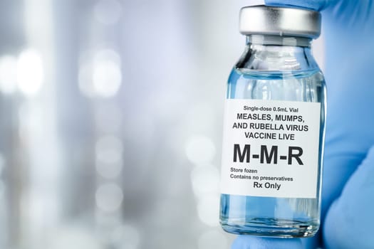 Healthcare concept with a hand in blue medical gloves holding MMR, measles, mumps, and rubella, vaccine vial