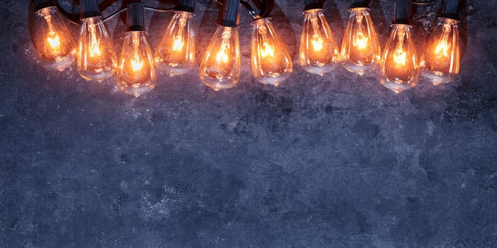 Row of lit string light bulbs glowing on dark grungy background.