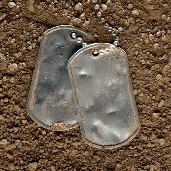 Dented and worn blank military dog tags fallen in dirt
