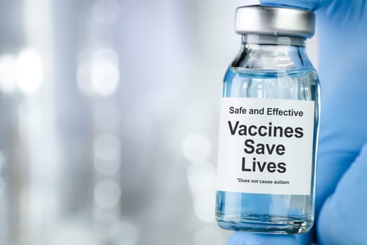 Healthcare concept with a hand in blue medical gloves holding a vaccine vial wtih the words Safe and Effective, Vaccines Save Lives, and does not cause autism