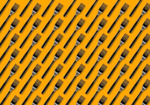 Many black plastic forks on blue background, top view. Disposable table wear concept. Creative top view pattern.