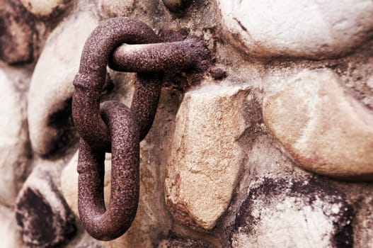 Rusty chain hanging on old stone wall