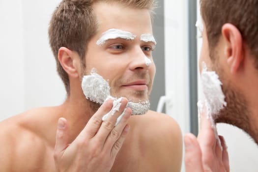 Man looking into the mirror and applying shaving foam