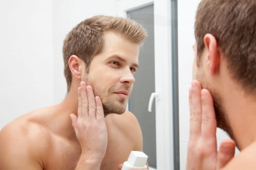 Man looking into the mirror and applying aftershave
