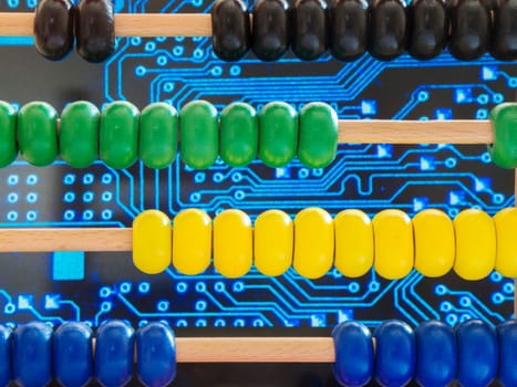 Close-up of a wooden abacus with colorful beads in front of traces of an electronic circuit board.