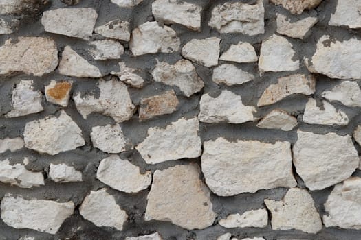 Natural off-white rough rock stone mixed with dark gray cement wall background surface close-up in the day. Close-up background of rough light gray stone and dark gray cement wall outside in the day.