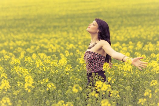 Attractive young beauty girl enjoying the warm sunny sun in nature rapeseed field takes time feeling sustainability and contemplation.