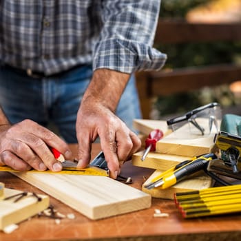Craftsman adult carpenter with a pencil and the joiner's team trace the cutting line on a wooden table. Housework do it yourself. Stock photography.