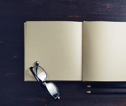 Photo of brochure with blank kraft paper pages, glasses and pencils on wooden background. Copy space for text. Flat lay.