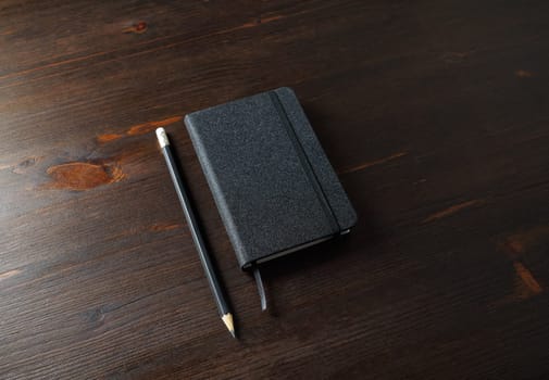 Photo of black notepad and pencil on wood table background.