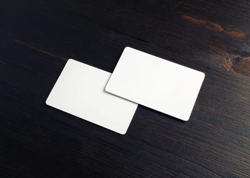 Two blank business cards on wood table background. Mockup for branding identity.
