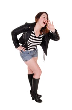 A young pretty woman standing in shorts and boots and a leather.jacket shouting with one hand on face, isolated for white background.