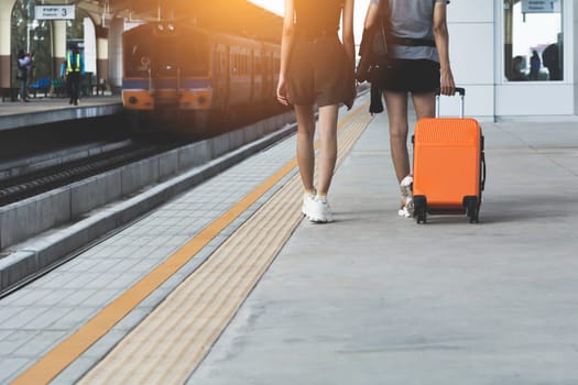 Woman dragging orange suitcase luggage bag, walking in train station. Travel concept.