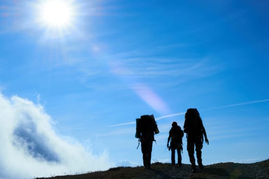 Silhouette of hiking friends against sun and blue sky