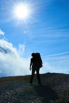 Silhouette of hiking woman against sun and blue sky