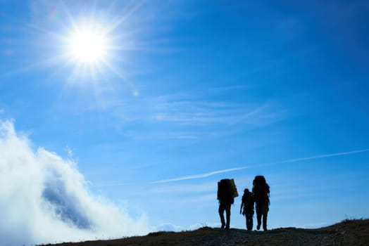 Silhouette of hiking friends against sun and blue sky