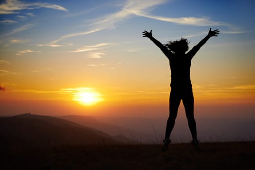 Silhouette of young woman jumping against sunset with blue sky