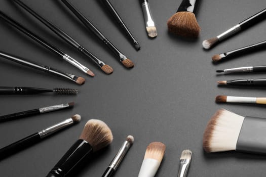 Different make-up brushes are in heart shape on gray background, loving make-up concept.