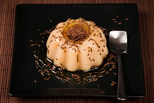 Cream pudding sweet dessert is served on black square shape plate on brown background.
