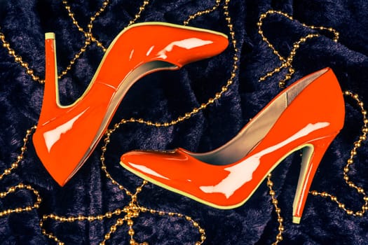Sexy orange high heels shoes are on dark blue fur background with golden pearl jewelry.
