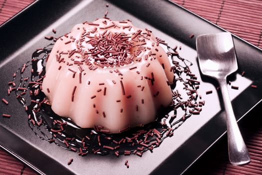 Pink pudding dessert with strawberry or raspberry taste on black plate.