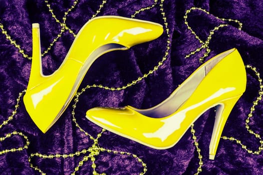 Sexy yellow high heels shoes are on dark purple fur background with yellow pearl jewelry.