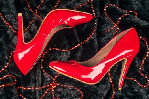 Sexy red high heels shoes are on black fur background with red pearl jewelry.