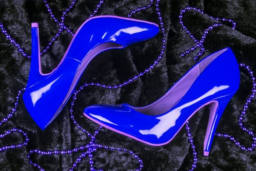 Sexy blue high heels shoes are on black fur background with purple pearl jewelry.