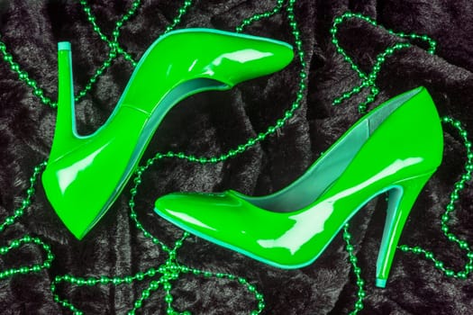 Sexy green high heels shoes are on black fur background with green pearl jewelry.