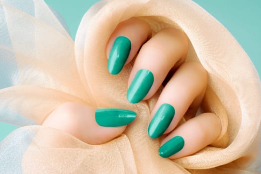 Female hand with turquoise nails is holding beige textile, nail care and manicure concept.