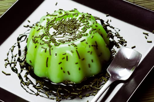 Green pudding sweet dessert from kiwi is served on black plate.