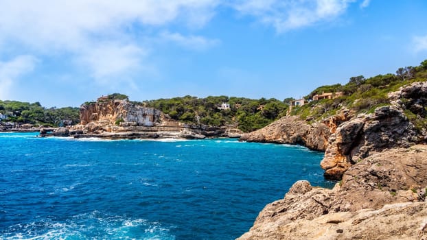 Houses on cliffs around beautiful beach, Cala Llombards in Mallorca, turquoise water and blue sky, Balearic Island, Spain