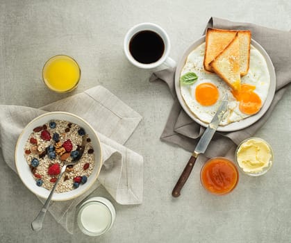 Breakfast served with oatmeal and fruits, fried eggs with bread and jam with butter on table top view. Healthy breakfast food