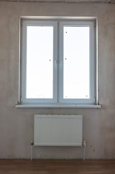 View of the window and the battery under the window in the interior of an unrepaired room